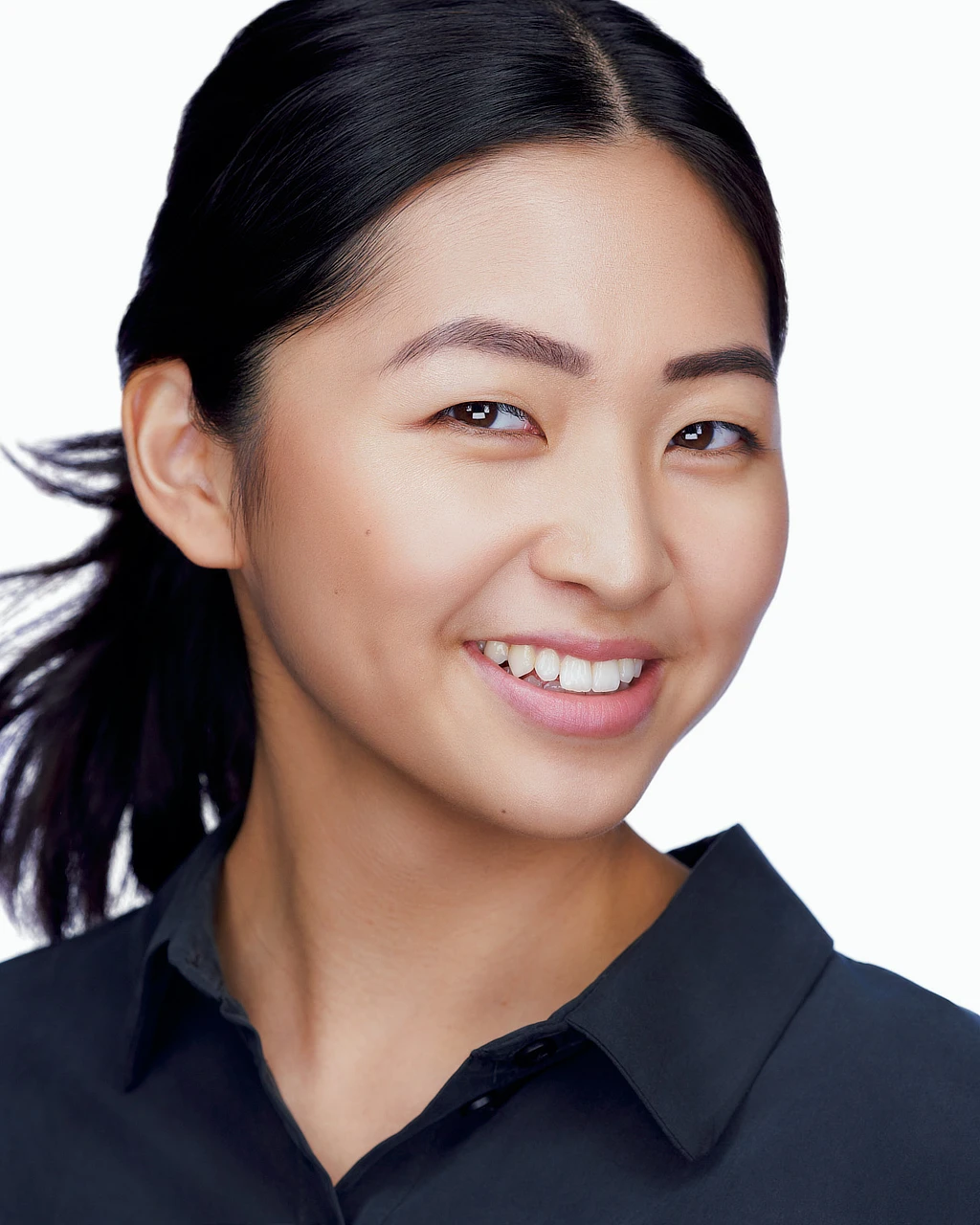 Woman with dark hair tied back smiling in a black collared shirt against a white background.
