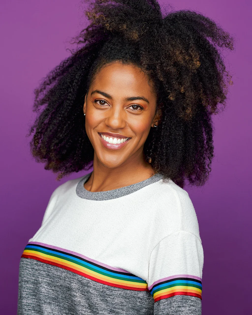 Smiling woman with natural curls photographed against a purple studio background in a colorful creative portrait.