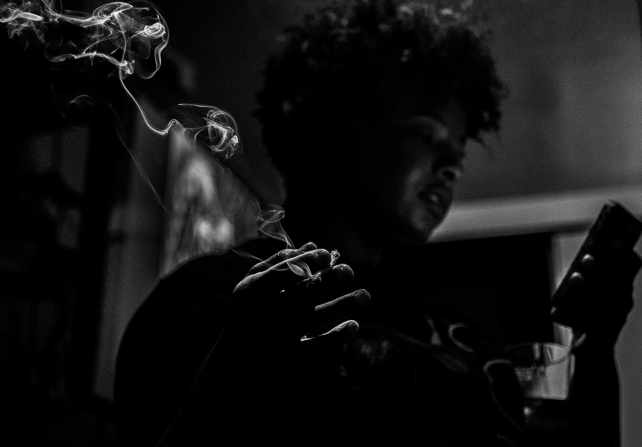 Moody black-and-white portrait with cigarette smoke drifting through the frame.