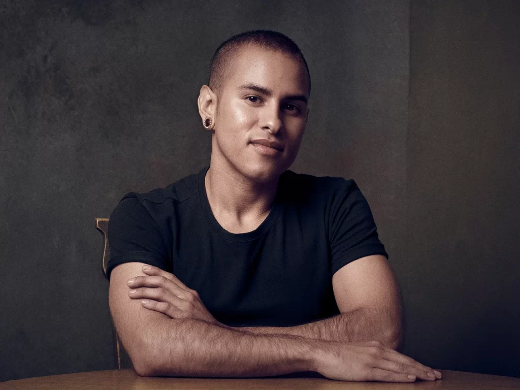Man in a black shirt seated at a table for a moody editorial portrait.