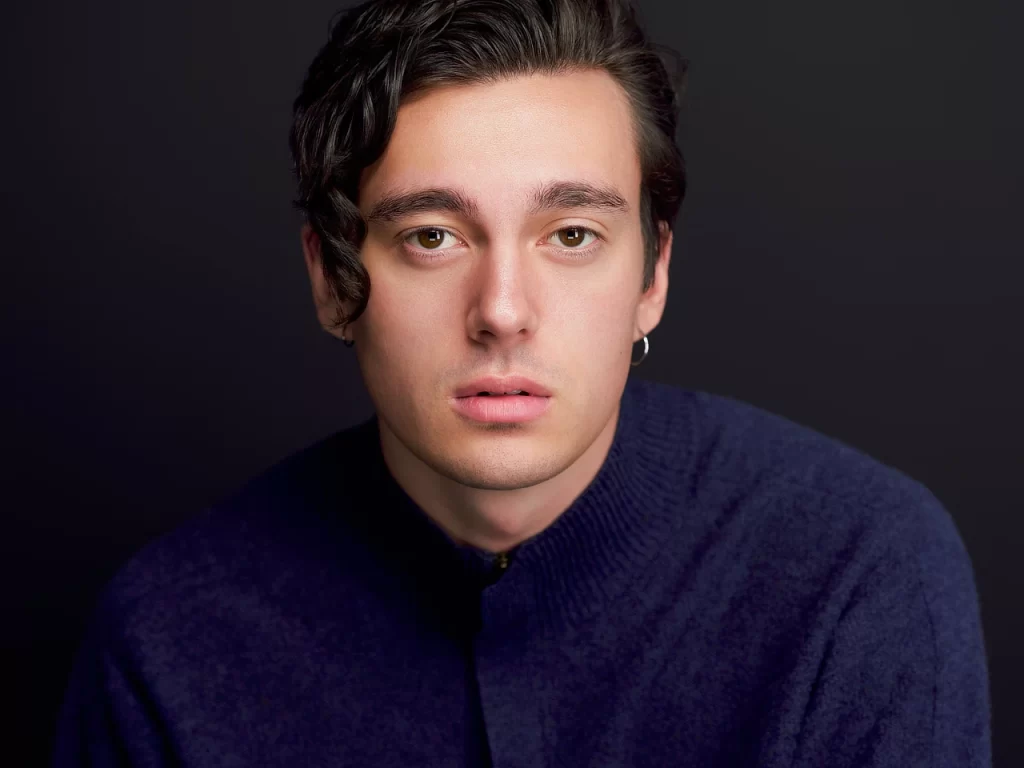 Young man in a dark sweater photographed against a moody studio background for an editorial portrait.