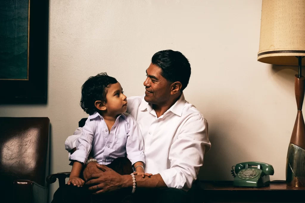 Father and young son seated together in a vintage room with a rotary phone and mid-century lamp.