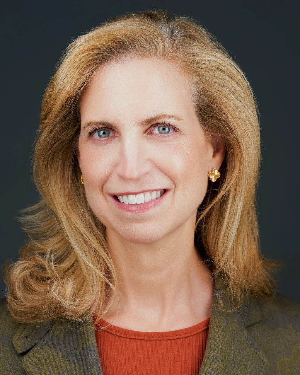 Finance professional in a bronze top photographed against a dark gray studio background.