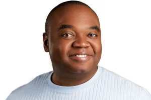 Henry smiling in a pale blue ribbed shirt against a white background.