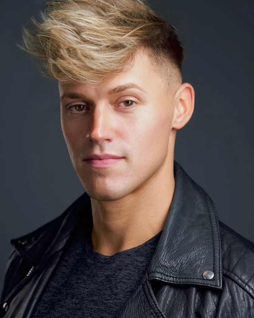 Joe Royal wearing a black leather jacket with a serious expression against a dark gray background