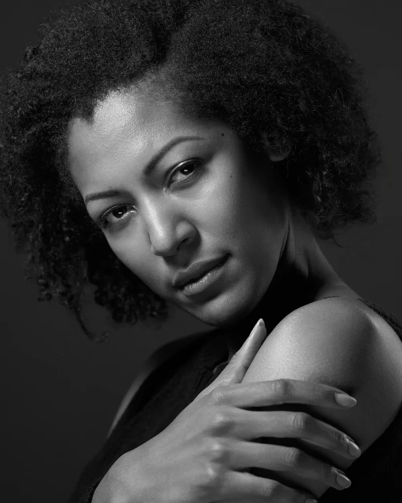 Black-and-white editorial modeling portrait of June with her hand resting across her shoulder.