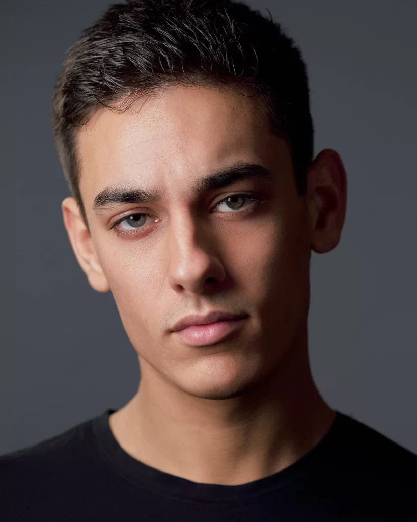 Clean male modeling headshot of Logan in a black shirt against a neutral gray studio background.