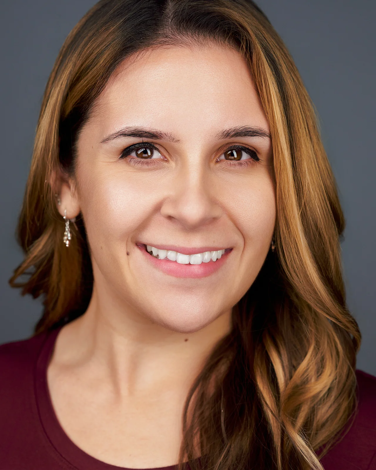 Headshot of a therapist smiling in a burgundy top against a gray background