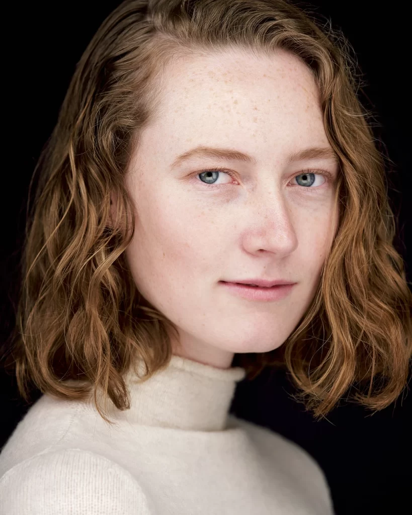 Natural modeling headshot of Sydney with freckles and red hair against a dark studio background.